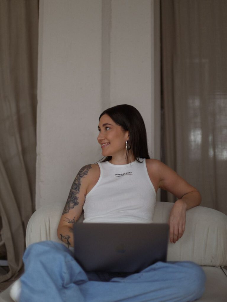 Alina, der Gründerin von the sweet socials: Sie sitzt auf einem Sessel, hat einen Laptop auf dem Schoss und schaut lächelnd zur Seite