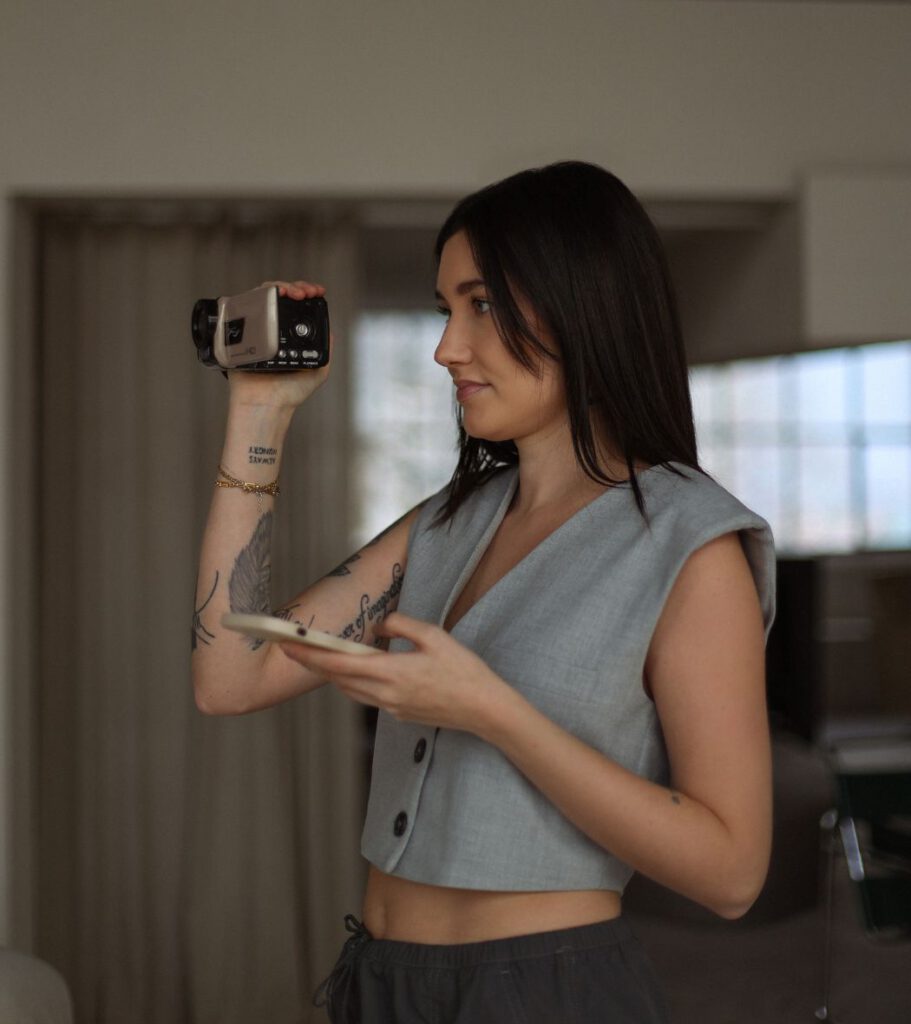 Alina von the sweet socials hält eine Kamera und ihr Handy in der Hand. Sie arbeitet konzentriert und schaut nicht in die Kamera